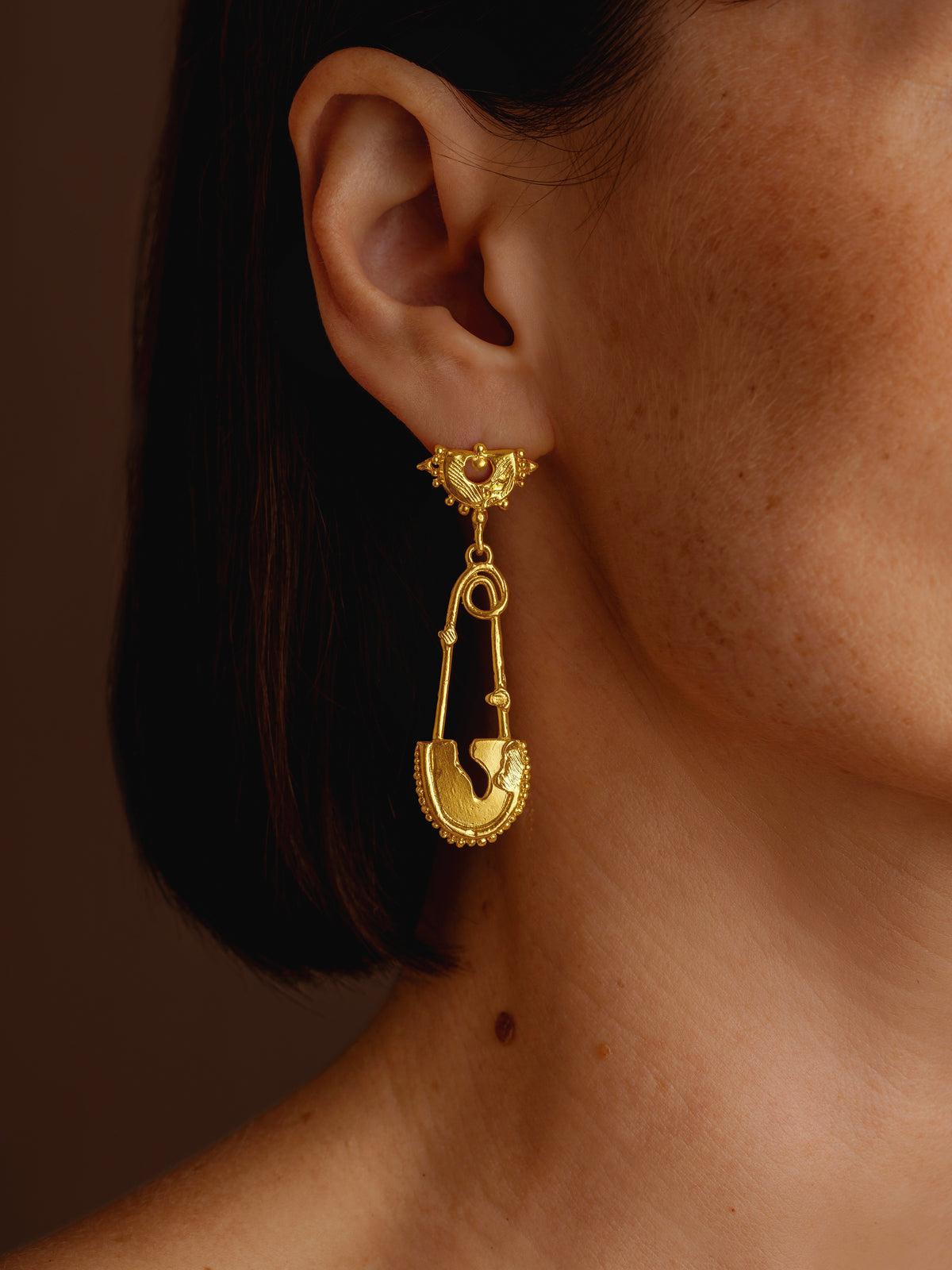 Close-up of ornate gold statement earring with dangling charm